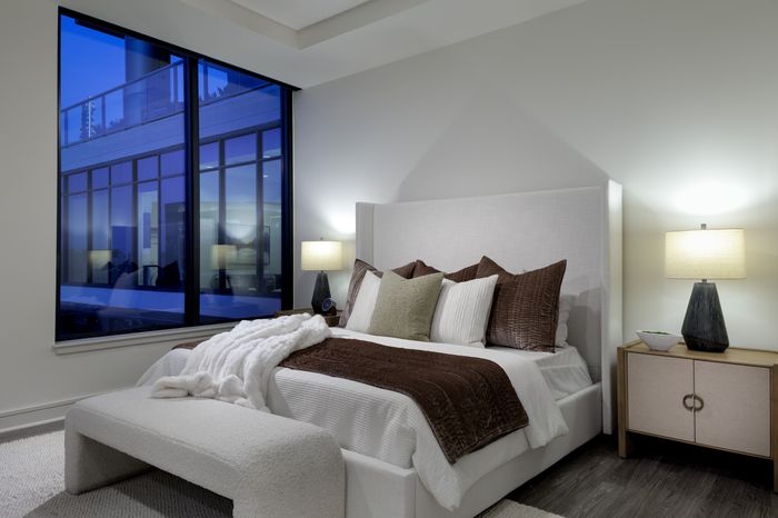 Elegant bedroom with modern furnishings, featuring a large window with city views, cozy bedding, and ambient lighting.