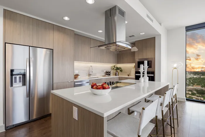 Modern kitchen featuring sleek cabinetry, stainless steel appliances, and a stylish island with bar seating. Large window offers a stunning view of the vibrant sunset.