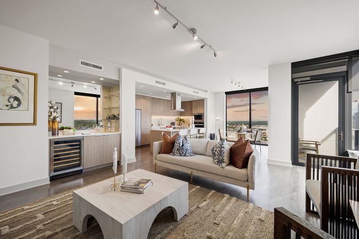 Luxurious open-concept apartment interior with a plush sofa and elegant decor, featuring a modern kitchen and dining area with stunning city views at sunset.
