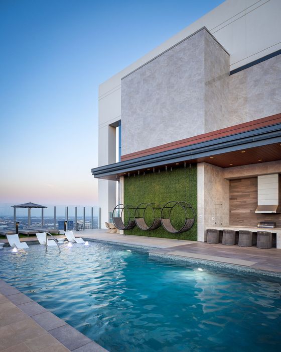 Luxurious rooftop pool area featuring modern hanging chairs, sleek poolside loungers, and an elegant outdoor kitchen with cityscape views.