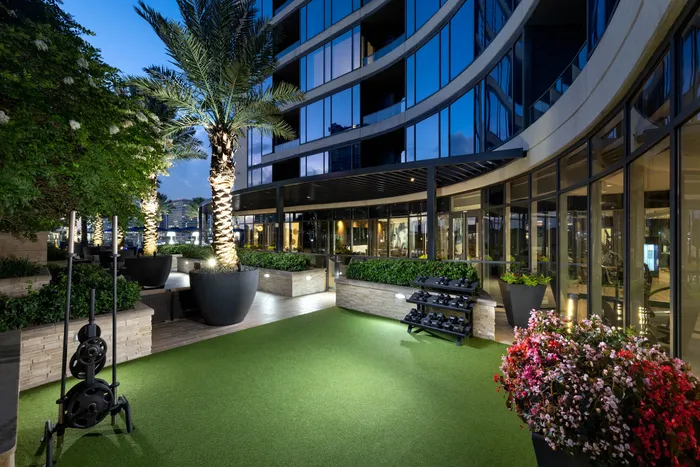 Luxurious apartment exterior with lush landscaped garden, modern glass facade, and well-lit palm trees.