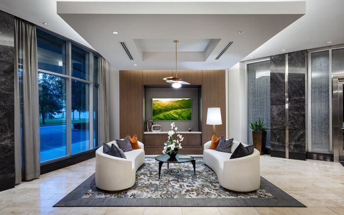 Elegant apartment lobby featuring modern white seating, a central coffee table with floral decor, and large windows for natural light.