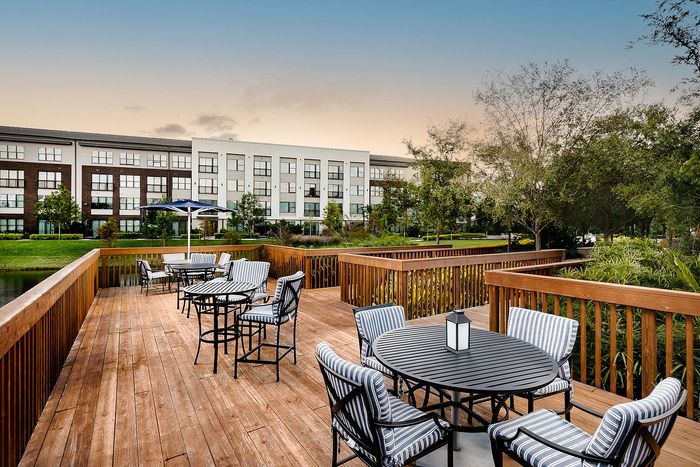 Charming outdoor deck area with stylish seating overlooking lush greenery and modern apartment complex.