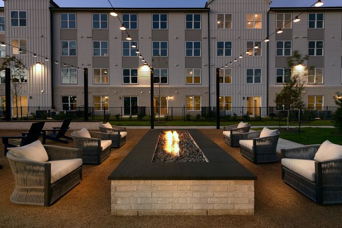 Chic outdoor patio with elegant seating around a warm fire pit, set against a stylish apartment building backdrop under twinkling lights.