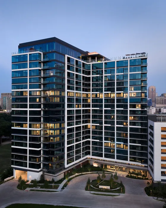 Modern high-rise apartment building with sleek glass facade and city views, surrounded by lush greenery.