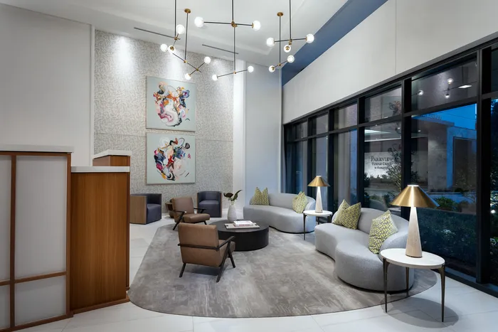 Chic apartment lobby with modern artwork, elegant lighting, and plush seating, featuring large windows for natural light.