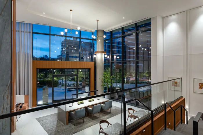 Luxurious apartment lobby with floor-to-ceiling windows showcasing city views, elegant lighting fixtures, and modern seating area.