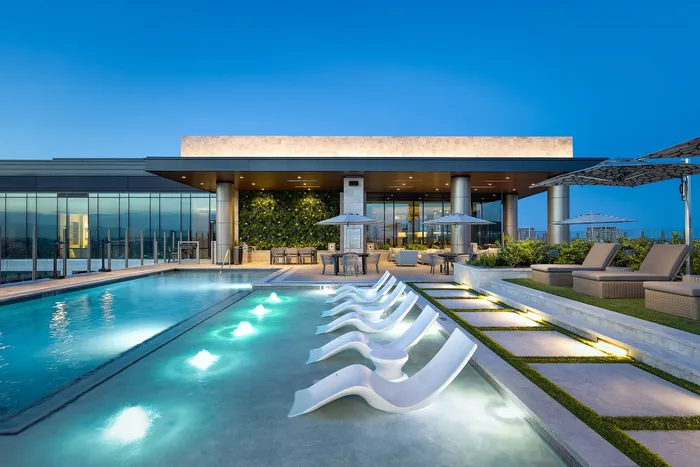 Luxurious rooftop pool area with stylish lounge chairs, modern greenery wall, and sleek glass windows, offering a serene urban escape.