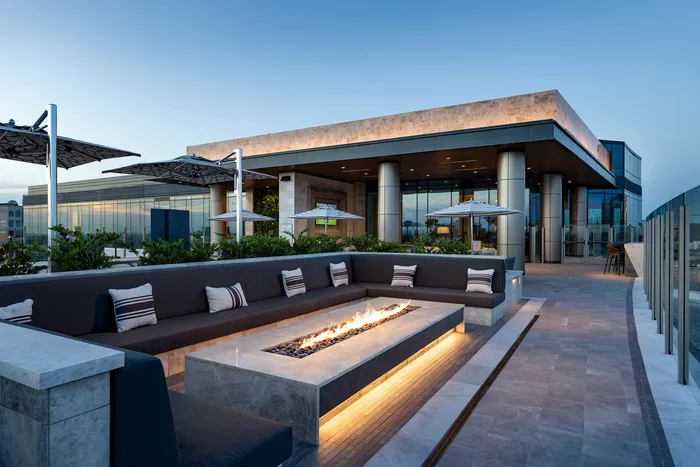 Luxury rooftop terrace featuring a modern fire pit with elegant seating, surrounded by lush greenery and stylish architecture.