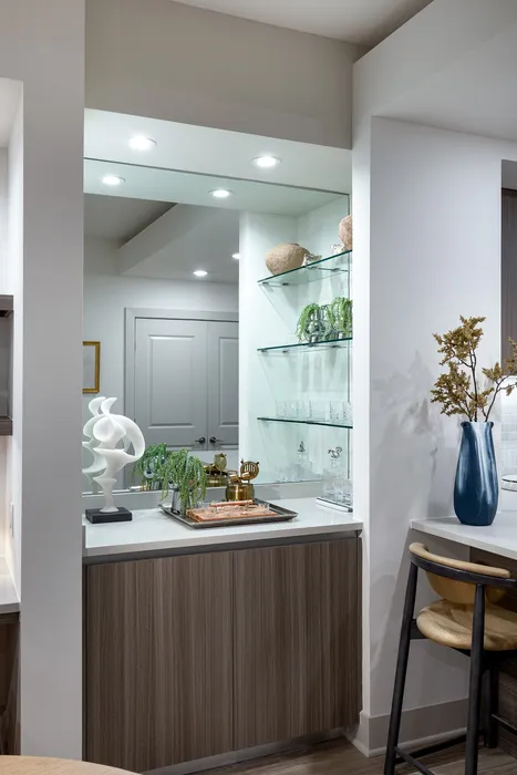 Chic modern kitchen corner featuring elegant shelving with decorative accents, stylish barstool seating, and warm wood cabinetry.