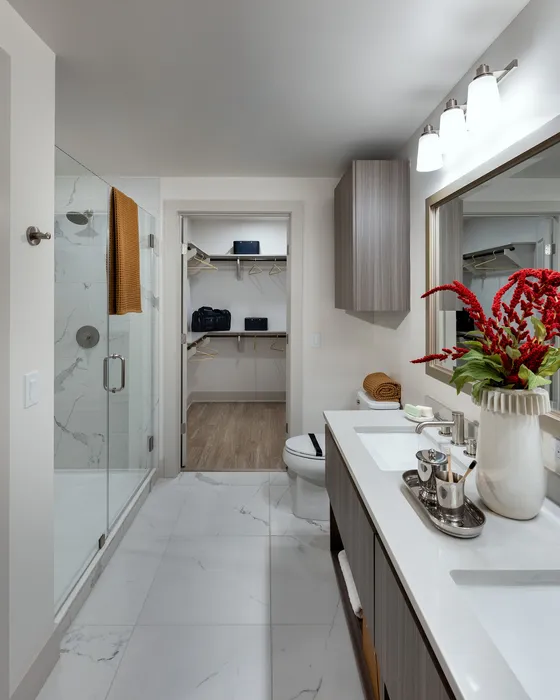 Elegant bathroom with marble tiles, a sleek glass shower, and a modern double vanity, leading to a spacious walk-in closet.