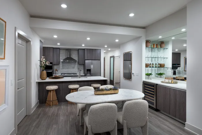 Modern kitchen with sleek dark cabinetry, a spacious marble island, and elegant dining area featuring plush white chairs, ideal for entertaining.