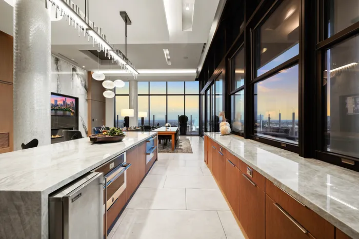 Luxurious open-concept kitchen and dining area with elegant marble countertops, modern appliances, and expansive city skyline views through floor-to-ceiling windows.