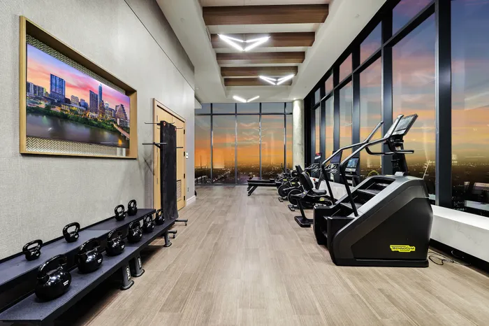 Luxury fitness room with modern exercise equipment, floor-to-ceiling windows, and captivating sunset city views.