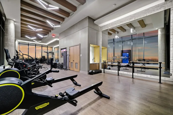 Sleek, modern fitness center with state-of-the-art gym equipment, mirrored walls, and expansive city views at sunset.