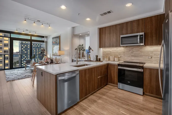 Modern open-concept kitchen with sleek wooden cabinetry, stainless steel appliances, and spacious countertop, seamlessly leading into a chic living area with large windows overlooking city views.