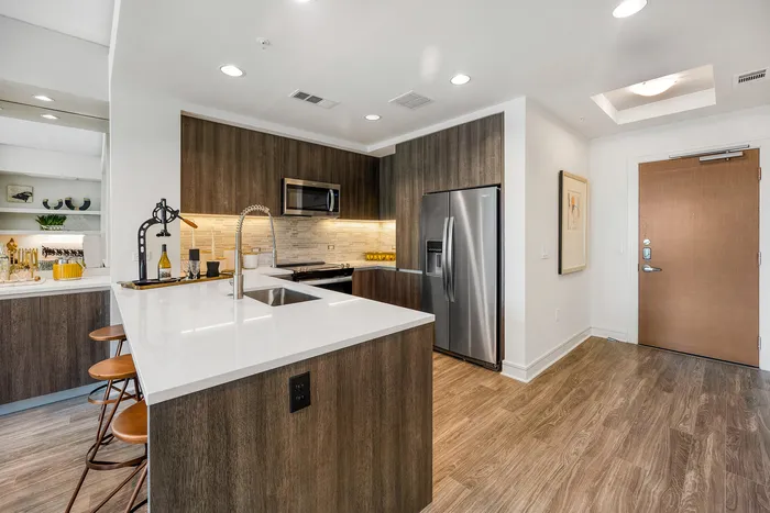 Modern kitchen with stylish dark wood cabinets, stainless steel appliances, and sleek countertops, featuring elegant bar seating and warm lighting.