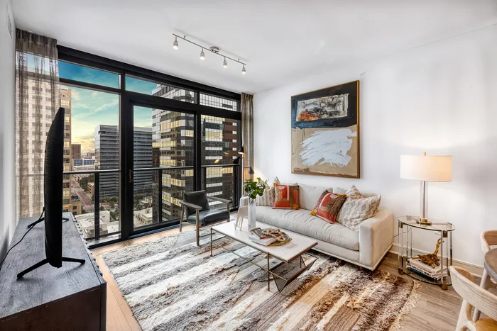 Chic, modern living room with floor-to-ceiling windows offering stunning city views, stylish decor, and a cozy seating area.