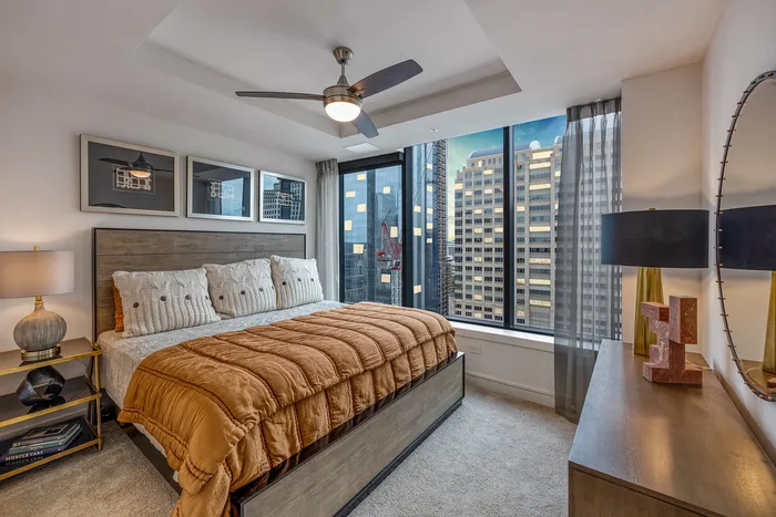 Chic urban bedroom with modern decor, featuring large windows showcasing a stunning city skyline view.