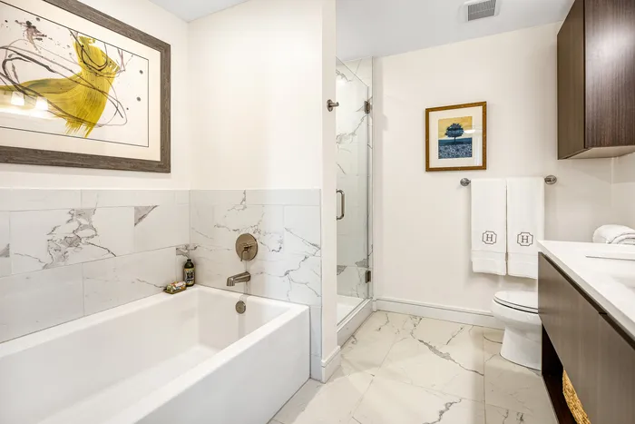 Elegant bathroom featuring luxurious marble tiles, a spacious tub, and a modern glass shower with stylish decor.
