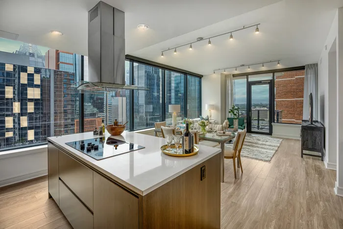 Chic open-plan apartment with modern kitchen island, elegant dining area, and floor-to-ceiling windows offering stunning city views.