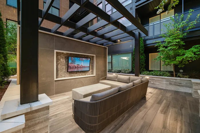 Modern outdoor lounge area with sleek design, featuring a plush sofa, wall-mounted TV, and stylish pergola.