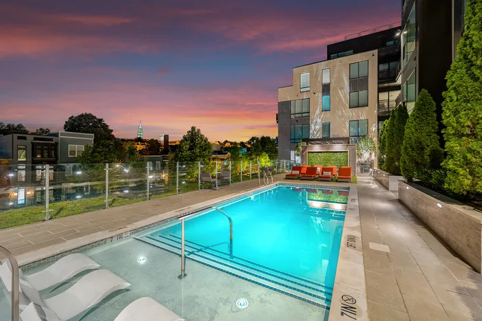 Luxurious evening poolside view with modern apartment building, elegant lounge chairs, and vibrant sunset backdrop.