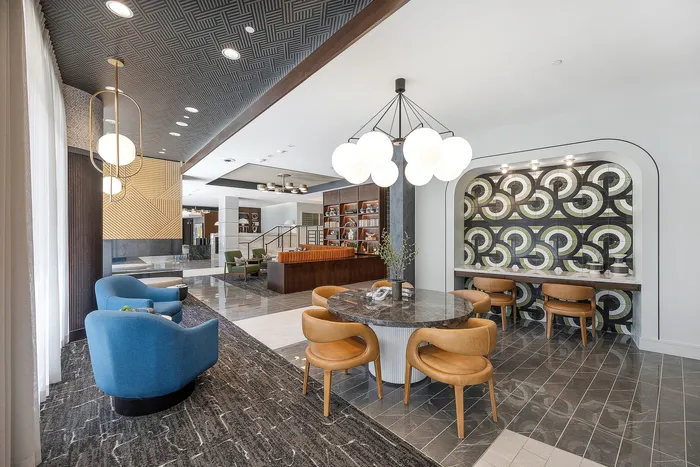 Modern apartment lounge area featuring elegant blue and tan seating, chic lighting fixtures, and stylish geometric wall patterns.