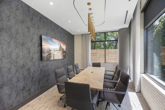 Modern and inviting conference room featuring stylish gray chairs, a sleek wooden table, and large windows offering natural light and a view of lush greenery.
