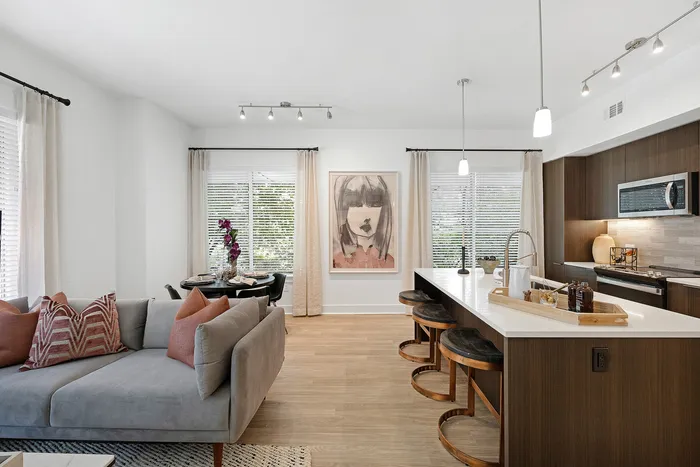 Modern open-concept living area with a chic kitchen island, cozy sofa, and elegant dining setup by large sunlit windows.