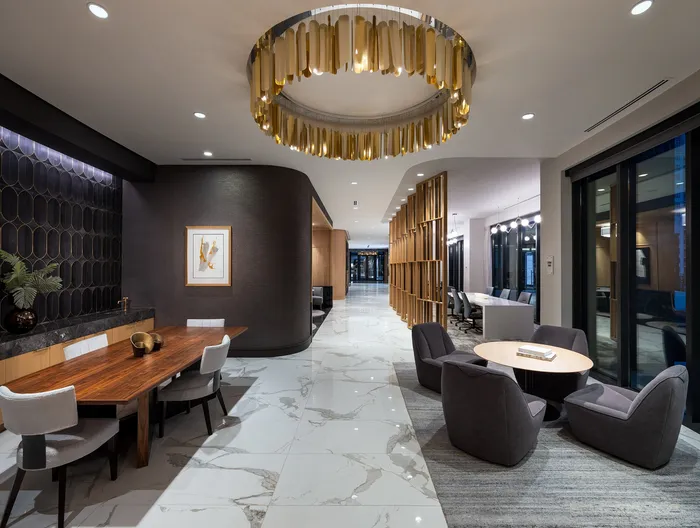 Elegant apartment lobby with modern seating areas, stylish wooden accents, and a striking gold chandelier.