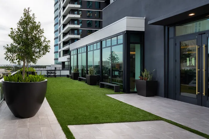 Modern high-rise building featuring a stylish rooftop terrace with lush greenery, large planters, and sleek glass doors, offering a tranquil urban oasis.