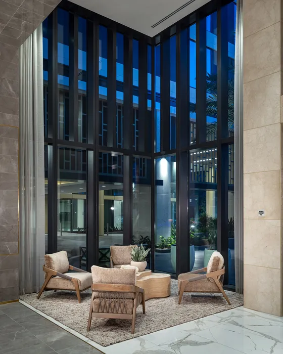 Elegant and modern lobby seating area with tall glass windows, stylish chairs, and a lush view, creating a welcoming atmosphere.