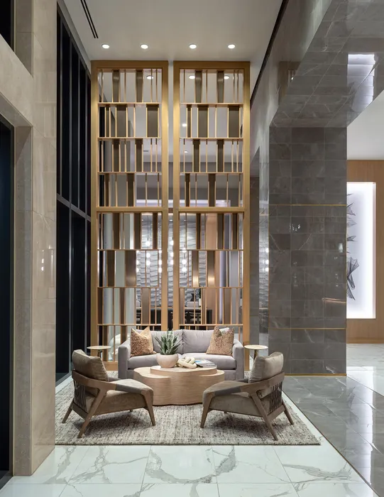 Luxurious apartment lobby featuring elegant seating area with modern decor, stylish wooden partition, and polished marble flooring.