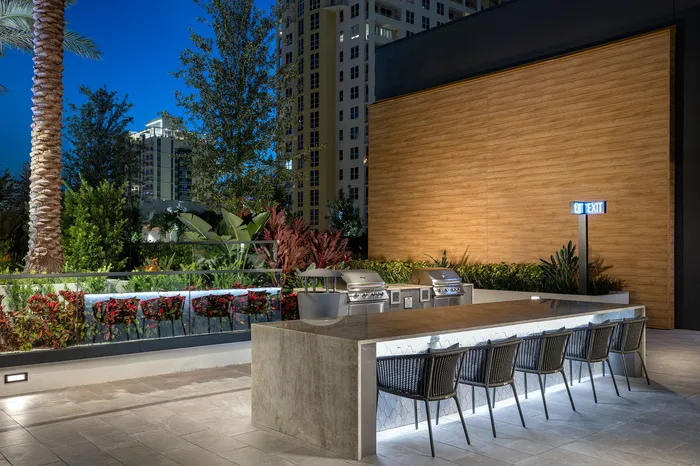 Elegant outdoor dining area featuring modern grills, stylish seating, and lush greenery, illuminated against a backdrop of cityscape at dusk.