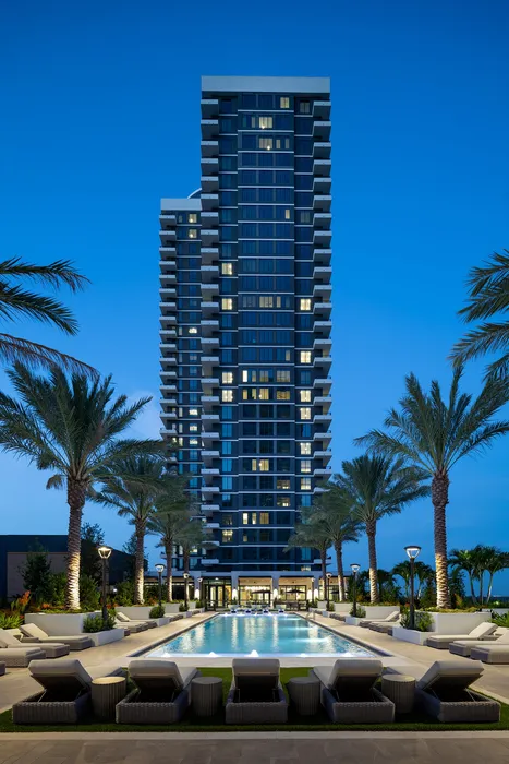 Luxurious high-rise apartment building with elegant outdoor pool and lush palm tree landscaping under a clear evening sky.