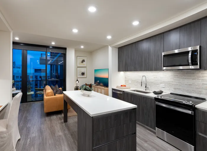 Elegant modern kitchen with sleek cabinetry, featuring a bright open living area and large windows showcasing city views.