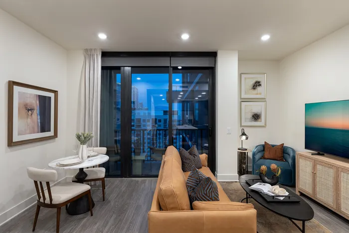 Modern living room with sleek furnishings, featuring a cozy couch, stylish armchair, elegant dining set, and a large window offering stunning city views.