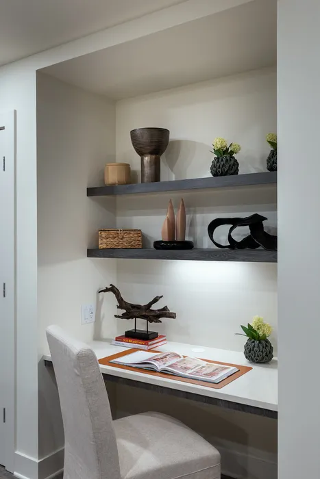Contemporary home office nook featuring elegant floating shelves with modern decor, a cozy chair, and a stylish desk setup.
