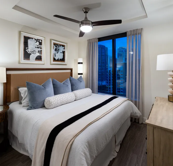 Modern bedroom with elegant decor, featuring a cozy bed, contemporary artwork, and a stunning city view through large windows.
