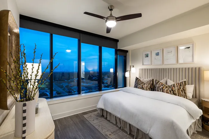 Luxurious bedroom with modern decor, featuring floor-to-ceiling windows offering stunning city views at twilight.