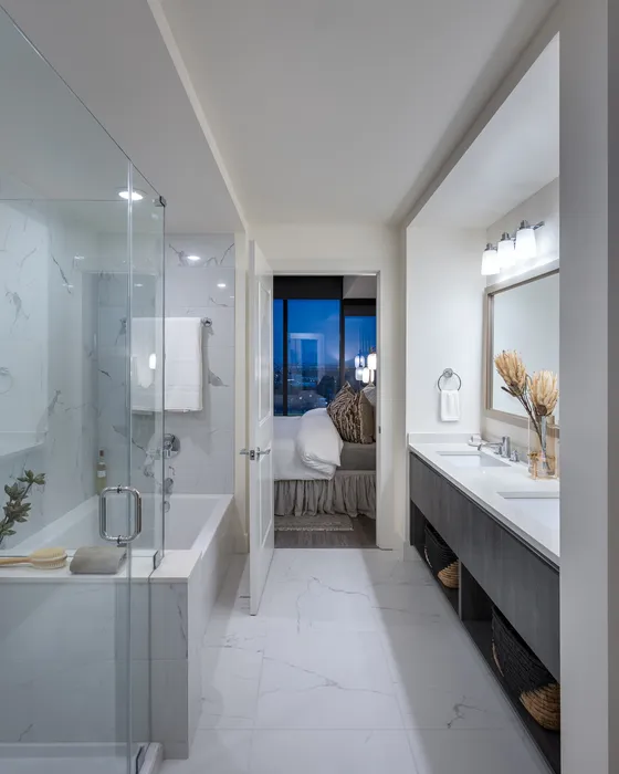 Luxurious bathroom with elegant marble tile, a spacious glass shower, and a sleek dual-sink vanity, offering a glimpse into a cozy bedroom with city views.