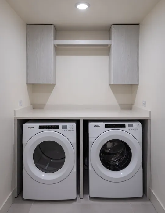 Modern laundry room with sleek white washer and dryer, spacious shelving, and elegant cabinetry.