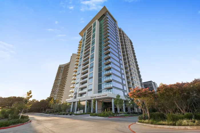 Elegant high-rise apartment building with modern architecture, large windows, and lush landscaping under a clear blue sky.