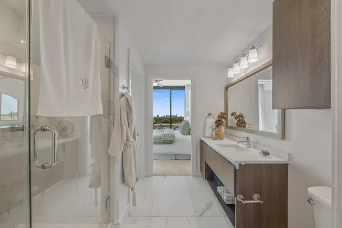 Luxurious modern bathroom with marble tiles, elegant fixtures, and a serene view leading to a cozy bedroom with large windows.