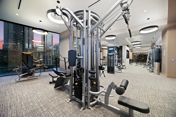 Luxurious apartment gym with state-of-the-art exercise equipment and large windows showcasing vibrant city views.
