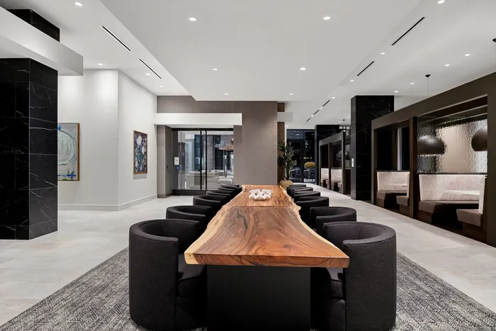 Elegant lounge area featuring a long, natural wood dining table surrounded by modern black chairs, complemented by stylish booths and contemporary artwork.