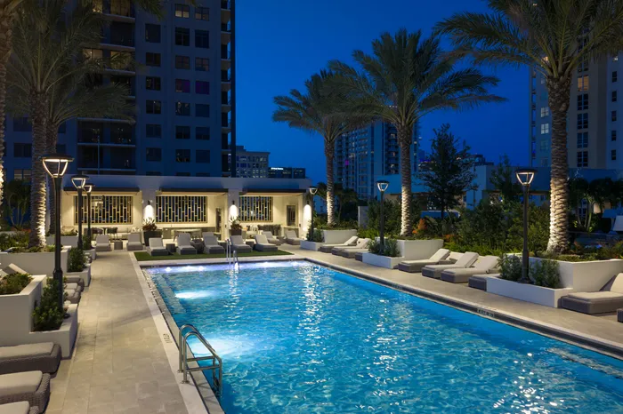 Luxurious apartment complex pool area beautifully illuminated at night, surrounded by elegant lounge chairs and palm trees, ideal for relaxation.