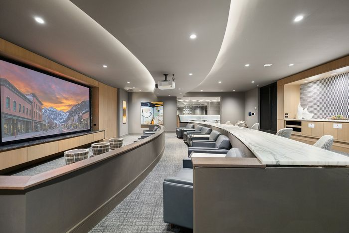 Luxurious home theater with curved seating, modern d&eacute;cor, and a large screen showcasing a mountain sunset scene.