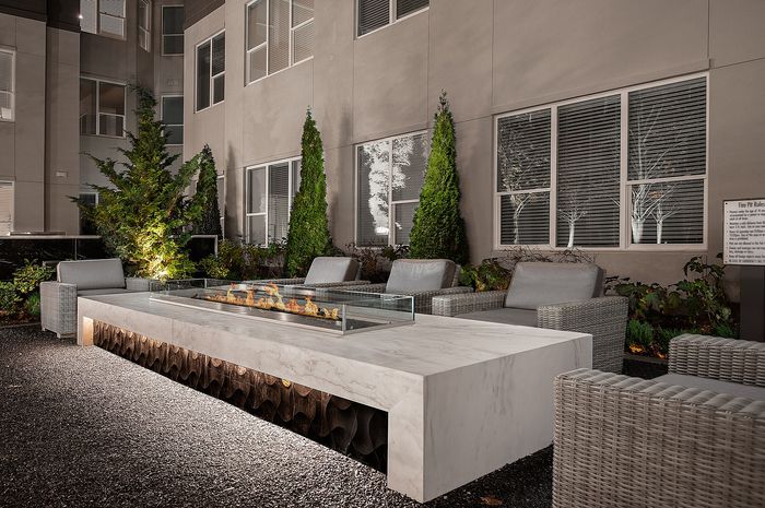 Elegant outdoor patio with modern fire pit, plush seating, and lush greenery, perfect for a cozy evening gathering.